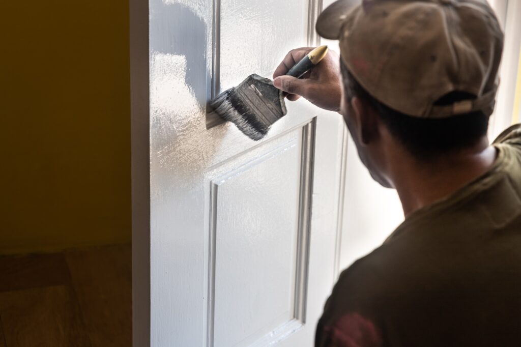 Person painting wooden white door with paint brush during home rennovation. Motion blur intended